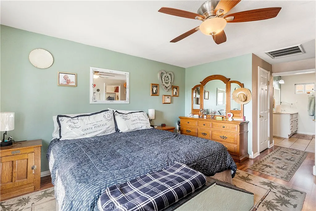 bedroom with king-size bed, wooden dresser with mirror, ceiling fan, and light green walls