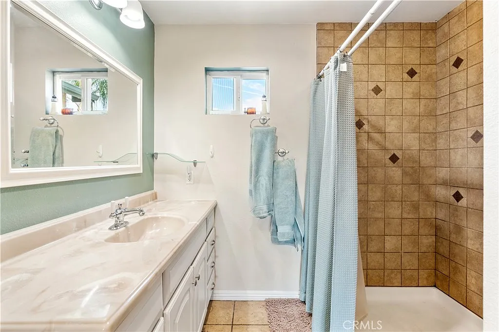 Bathroom with double sink vanity, large mirror, shower with beige tiles, and light blue curtains