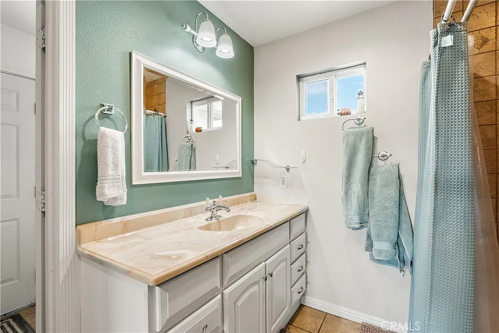 Bathroom with light-colored vanity, sink, large mirror, blue-green walls, and towels
