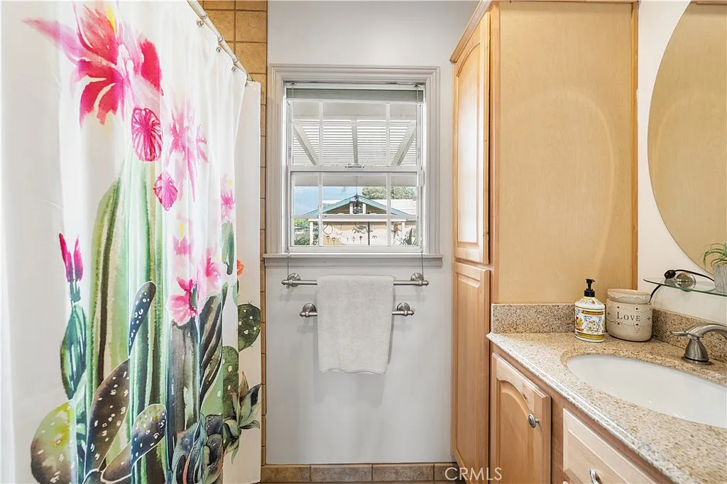 Bathroom with floral shower curtain, light wood cabinets, sink, and window