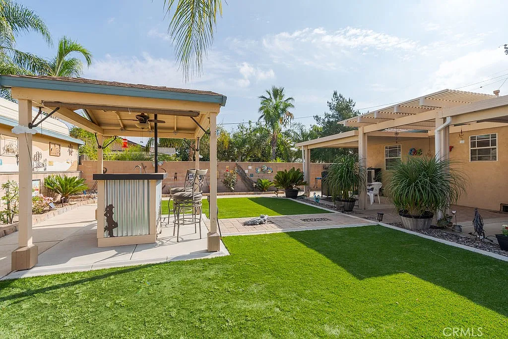Backyard with gazebo, bar area, and green lawn surrounded by plants and trees