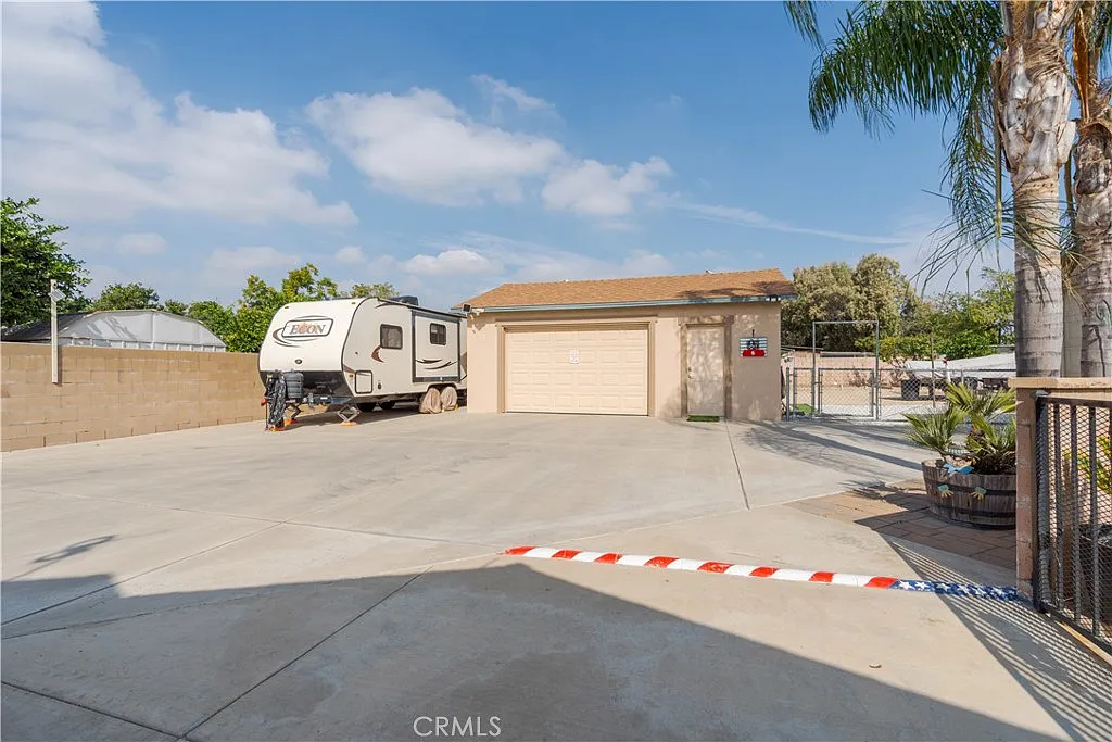 Driveway with RV next to garage, surrounded by palm trees and greenery