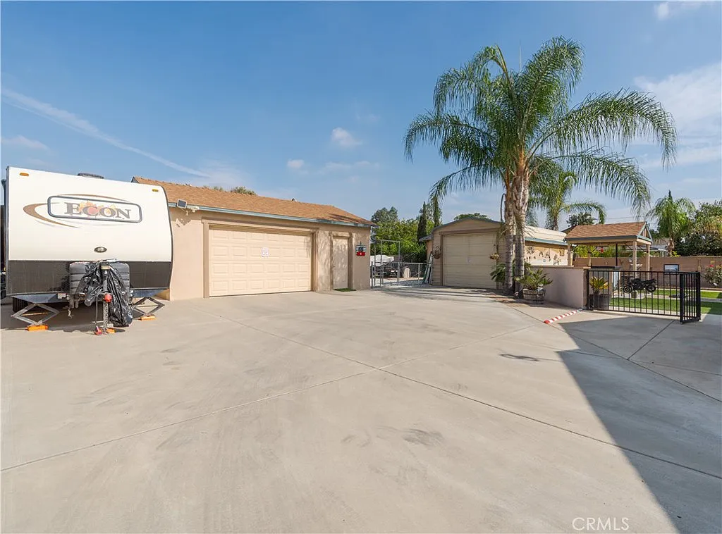 Driveway with RV, garages, palm trees, and house in background