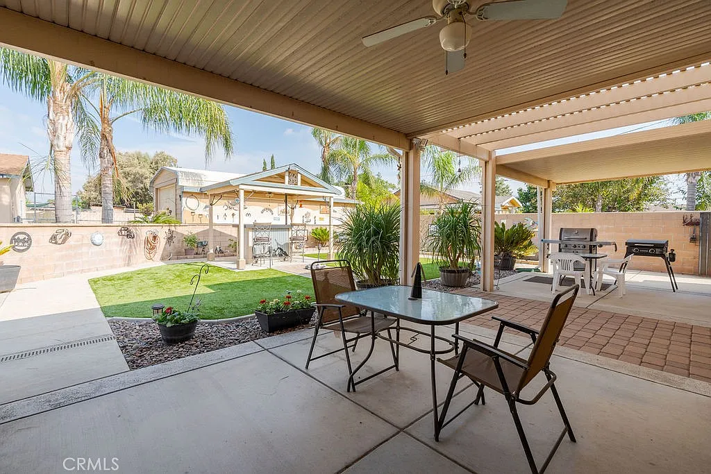 Backyard with covered patio, table and chairs, potted plants, and lawn with grill