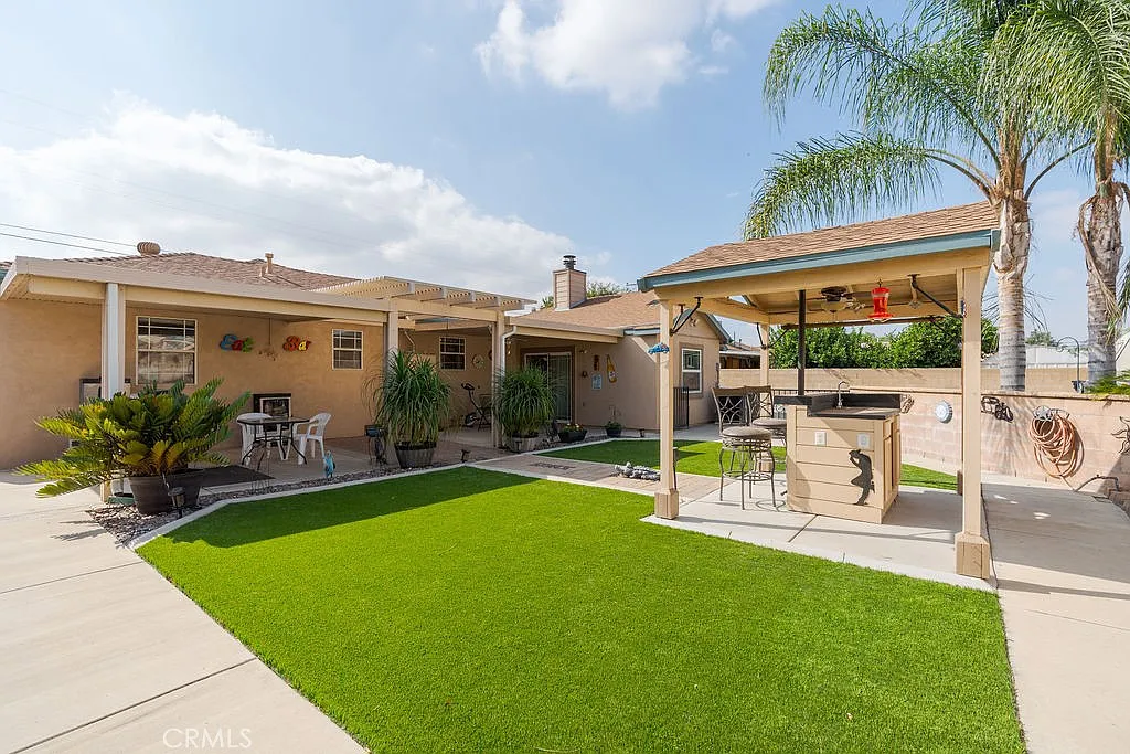 Backyard with green artificial grass, patio bar under gazebo, and potted plants