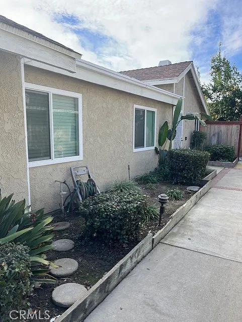 Beige house real estate with windows, concrete path, plants, and bushes.