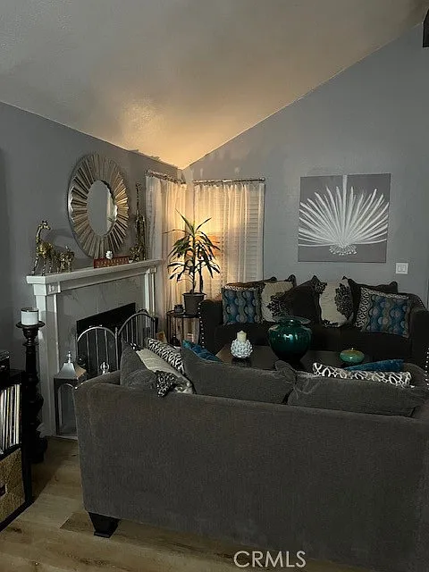 Living room with gray couch, pillows, fireplace, plants, wall art, and mantel decor.