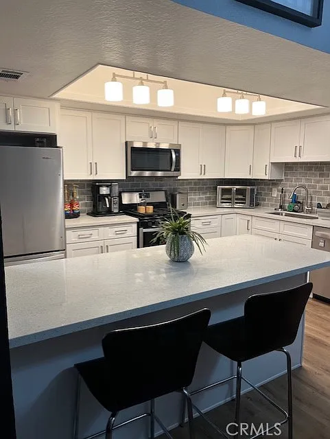 kitchen with white cabinets, stainless steel appliances, gray tile backsplash, and a large island with two black bar stools.