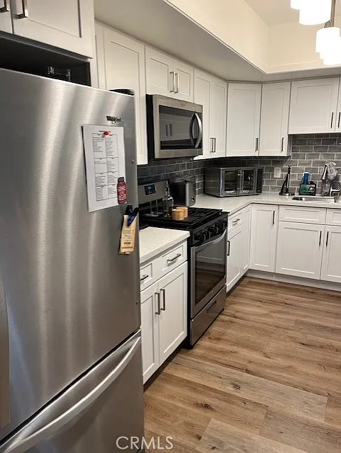 kitchen with stainless steel refrigerator and gas stove, white cabinets, and light wood floors.