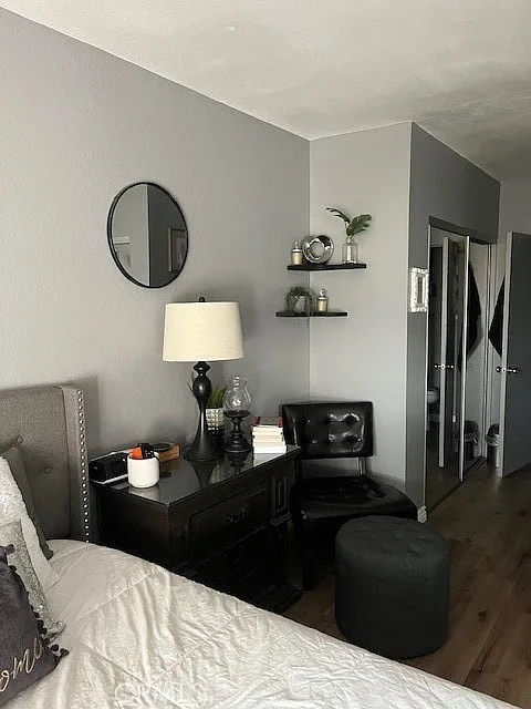 Bedroom with gray walls, white bed, round mirror, lamp, shelves, and chair.