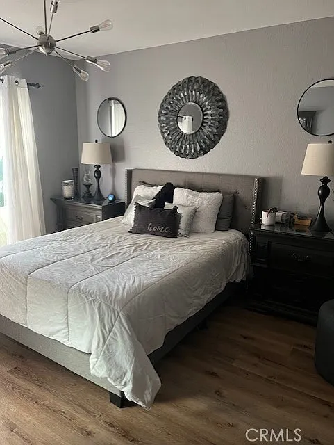 bedroom with a gray bed, white linens, bedside tables with lamps, round mirror above the bed, decorative walls, and wooden floors.