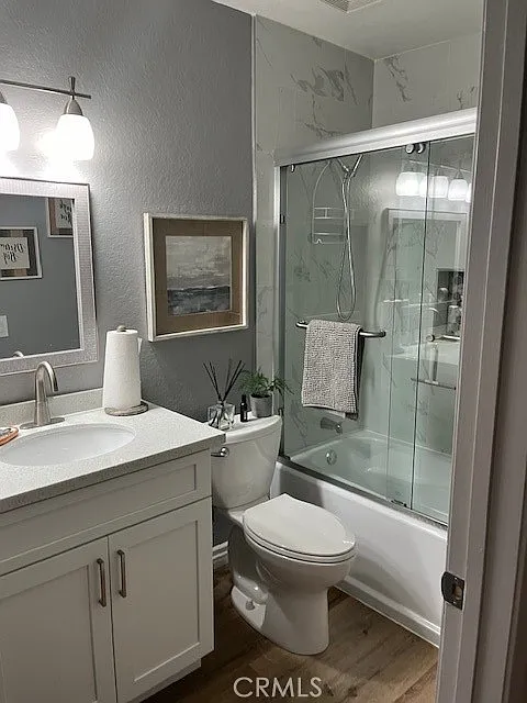 bathroom with a glass shower, white cabinets, toilet, sink with mirror, gray walls, and artwork on the counter.