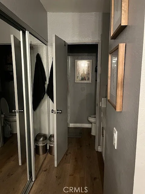 Narrow hallway with wood floor, bathroom door, wall picture, bins, and mirror closet.