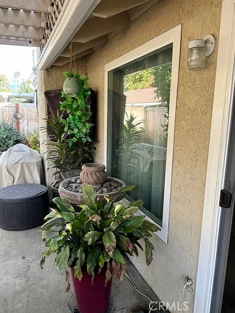 A patio with a window, green plants, a small water fountain, and potted greenery.