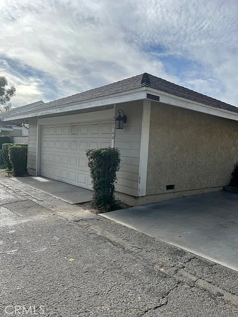 A garage with a closed door attached to a house, surrounded by shrubs and trees.