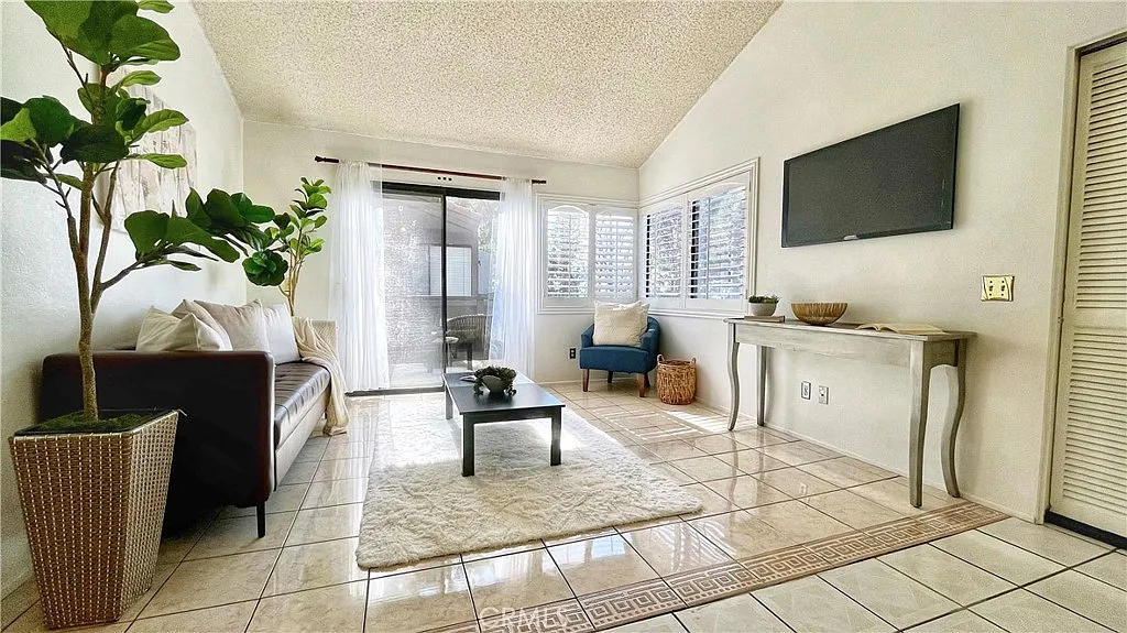 Living room with brown sofa, armchair, coffee table, tiled floor, sliding glass door, plants, and wall-mounted tv.