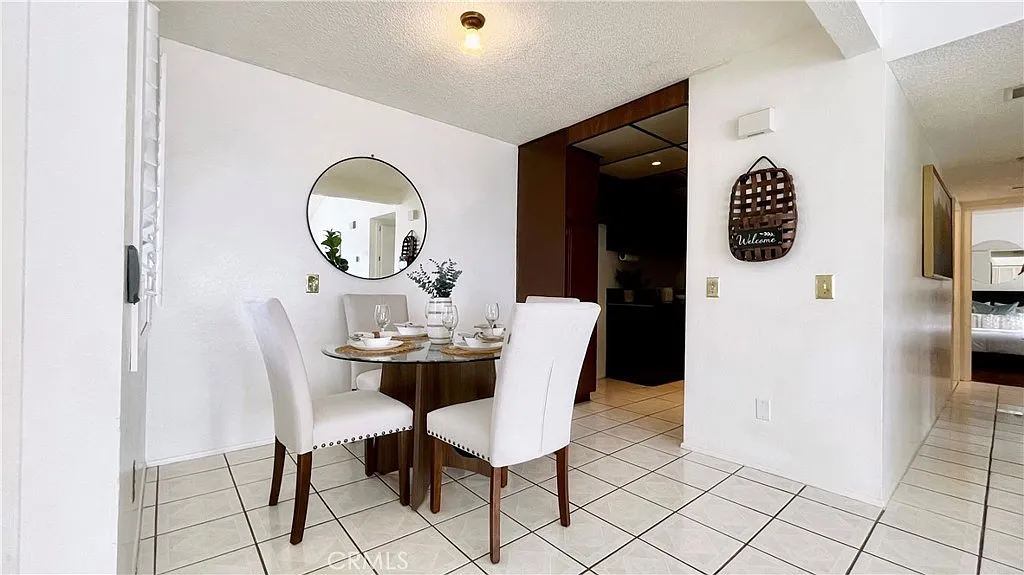 Small dining area with round table, two white chairs, circular wall mirror, white tile floor, and light walls.