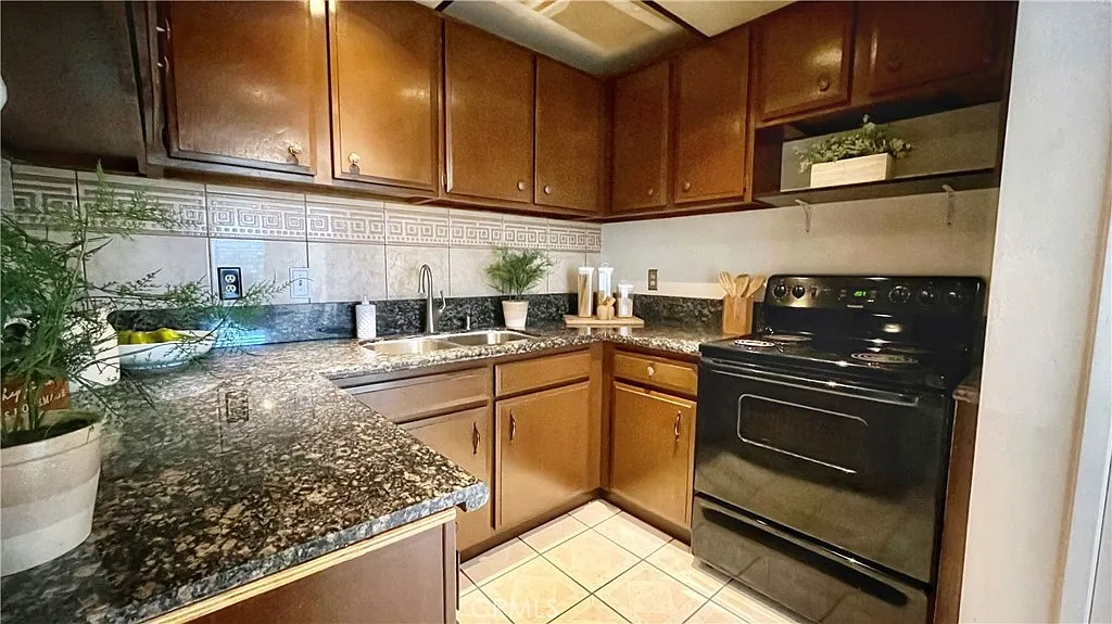Kitchen with dark wood cabinets, granite countertop, black oven, plates, and green plants.