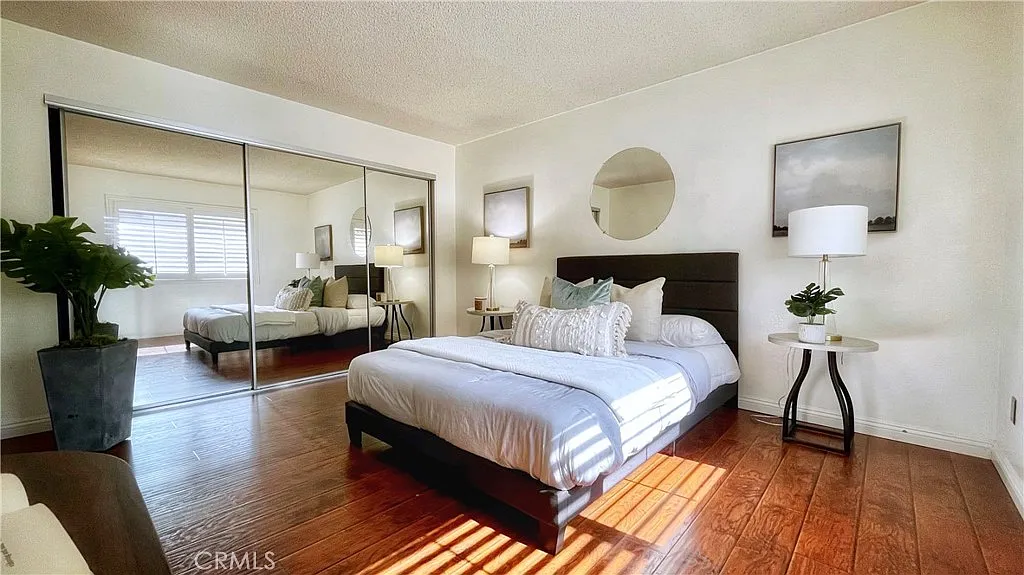 Bedroom with bed, soft linens, mirrored closet, round wall mirror, wooden floor