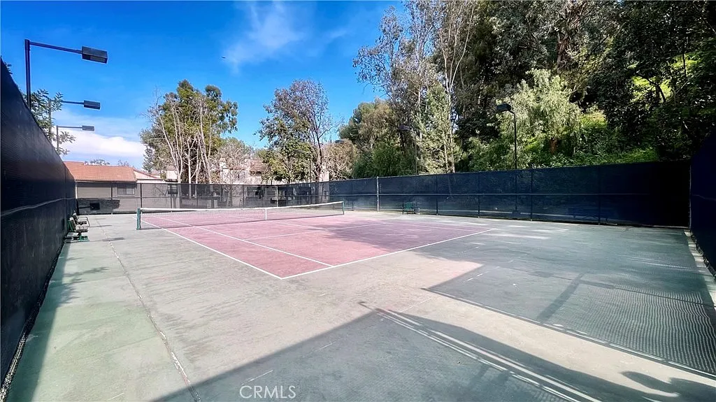 Tennis court with pink and gray surfaces, surrounded by trees