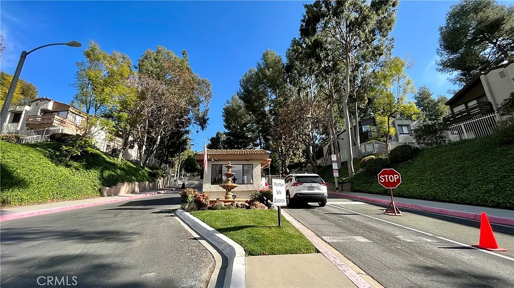 Gated entrance with stop sign, security booth, trees, and nearby residential buildings