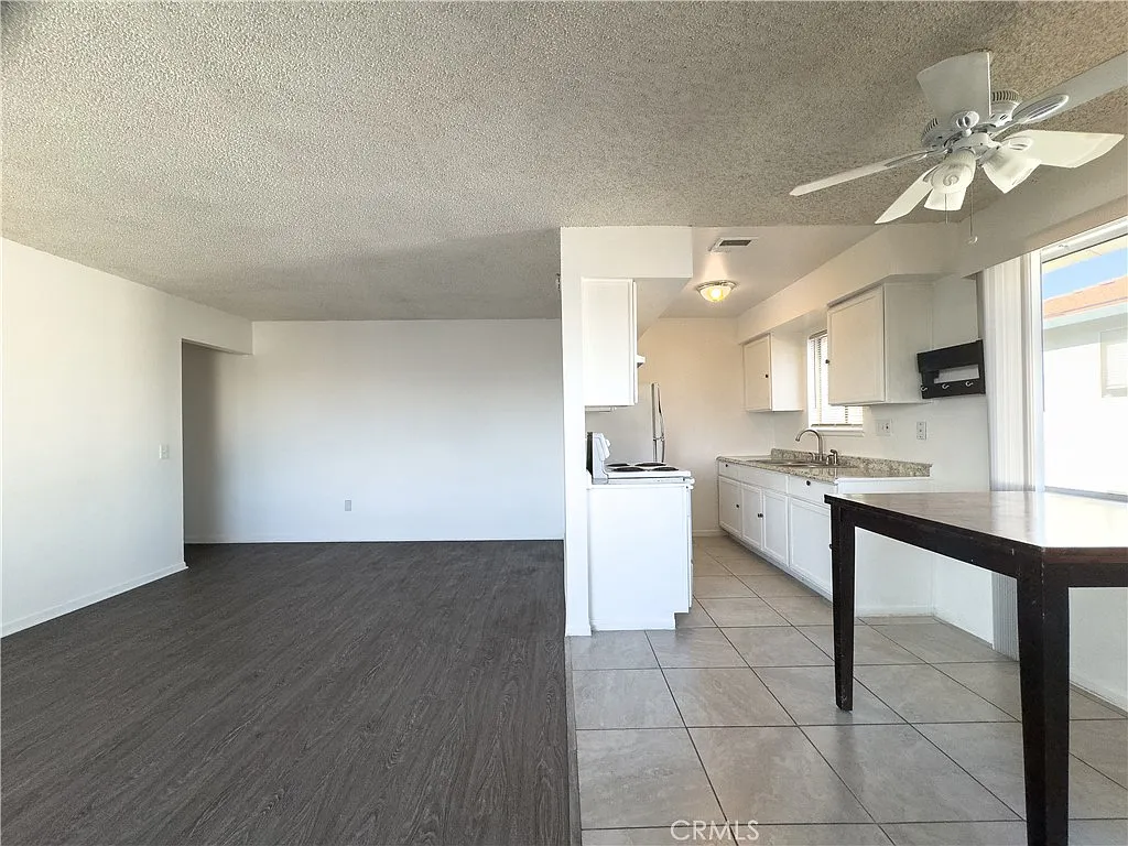 Interior view with kitchen of white cabinets and countertops, and living area with brown laminate floor.