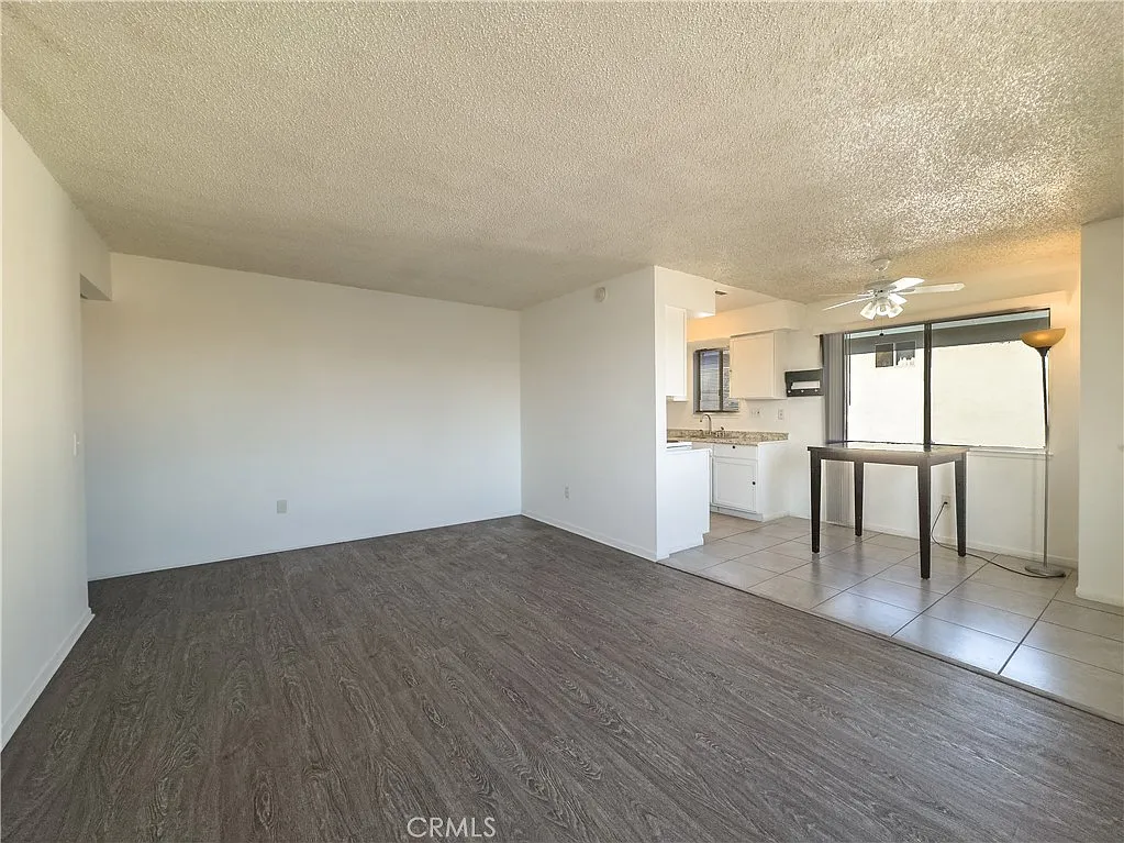 Living area with textured ceiling, hardwood floor, dining table, kitchen with light countertops, and window light.