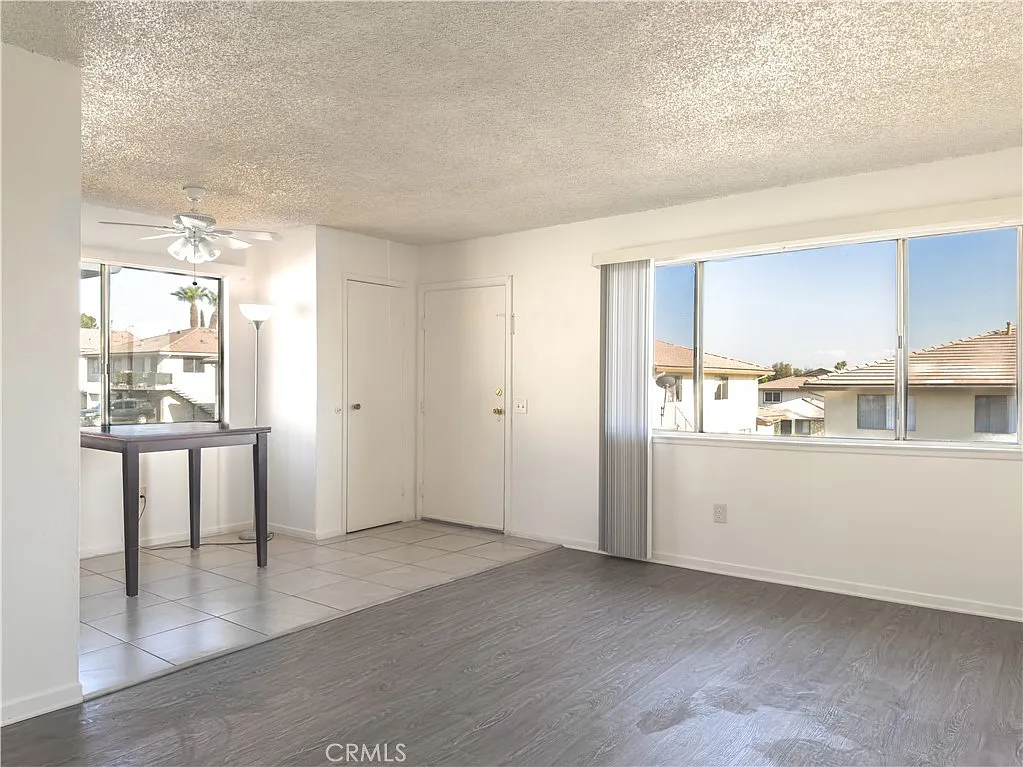 Open living space with window view, tiled floor, light walls, small table by window, and doors to other rooms.