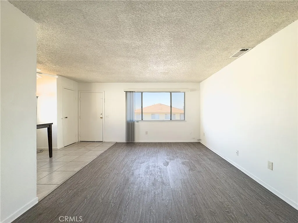 Empty living room with light walls, vinyl floor, window light, and doorway on the left.