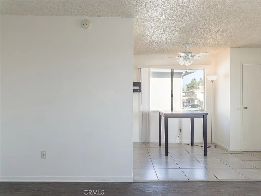 open living space with white wall, tiled floor, window light, small table, and corner lamp.
