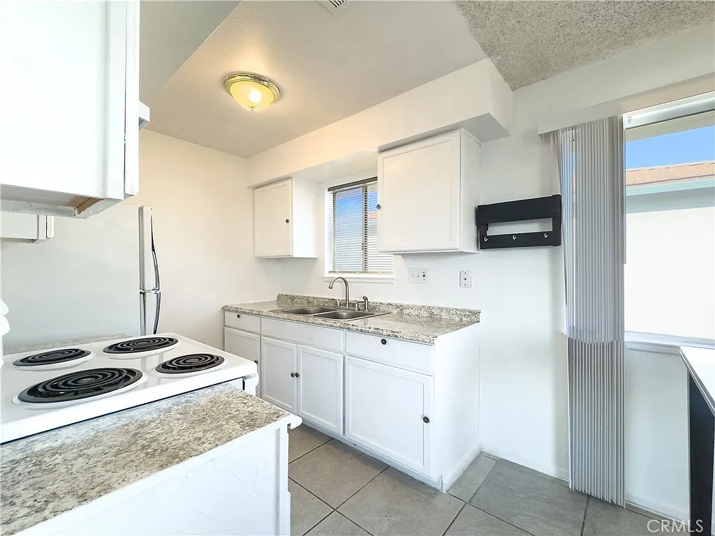 Kitchen with white cabinets, stainless steel refrigerator, granite countertops, four-burner stove, tile floor, and window light
