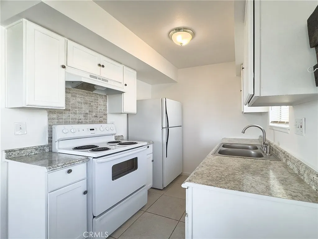 Kitchen with double sink, granite countertops, window with blinds, table, light walls, and tiled floor.