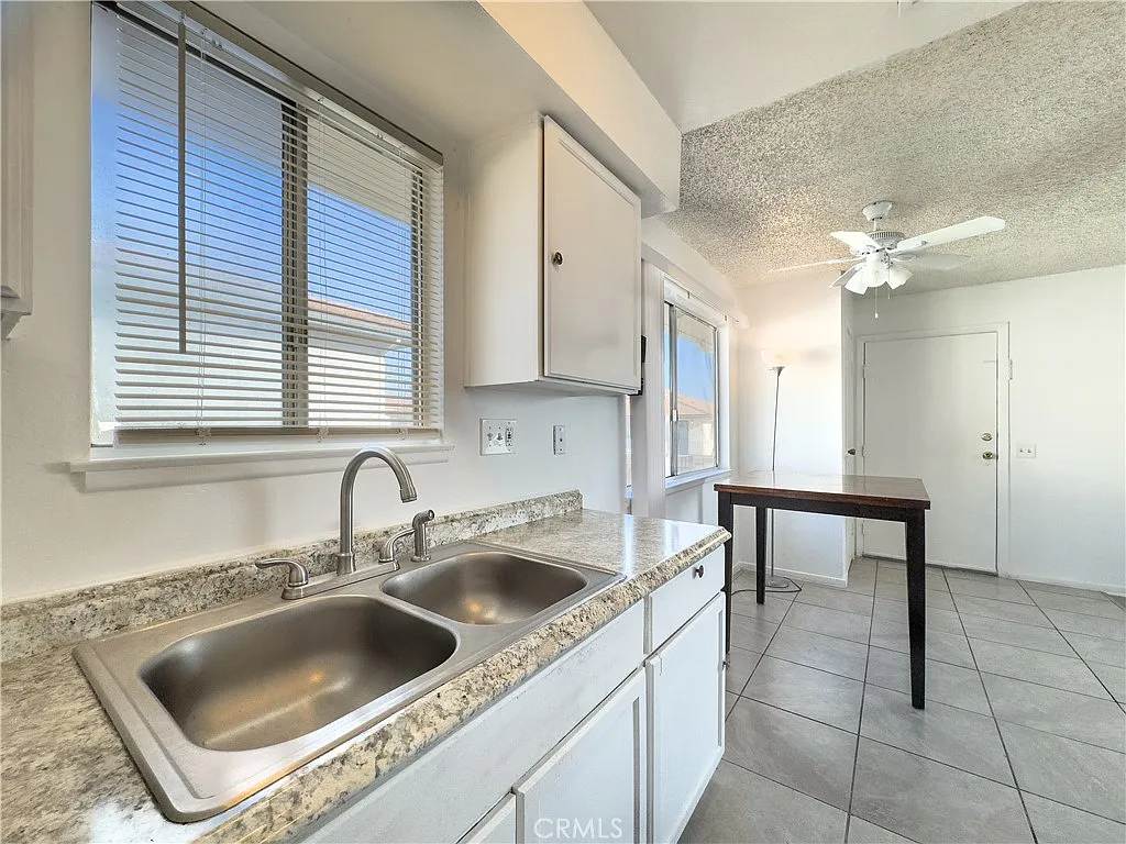Kitchen with double sink, granite countertops, window with blinds, table, light walls, and tiled floor.
