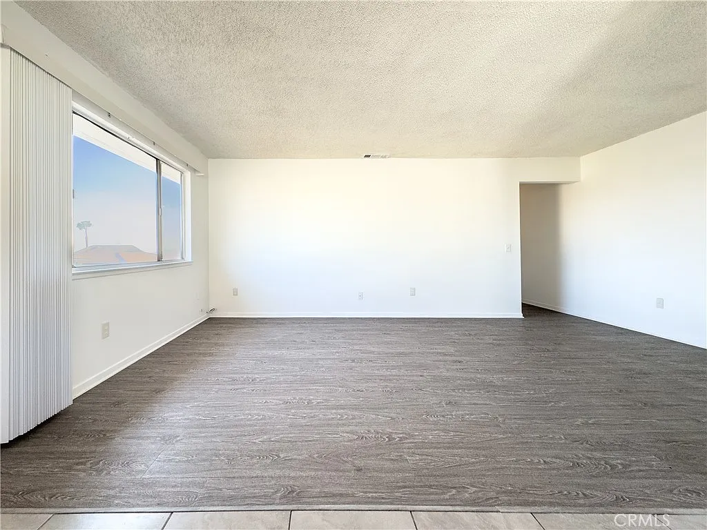 Empty room with white walls, light wood floor, large window, and doorway to another area.