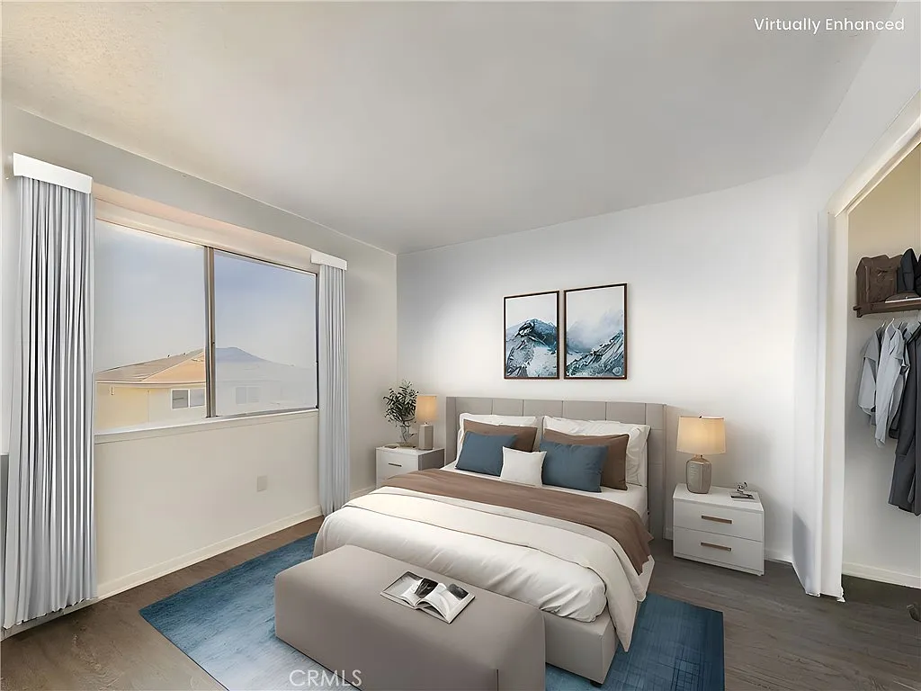 Bedroom with blue and beige bed, bedside lamps, wall pictures, window with gray curtains, blue rug, and wooden floor.
