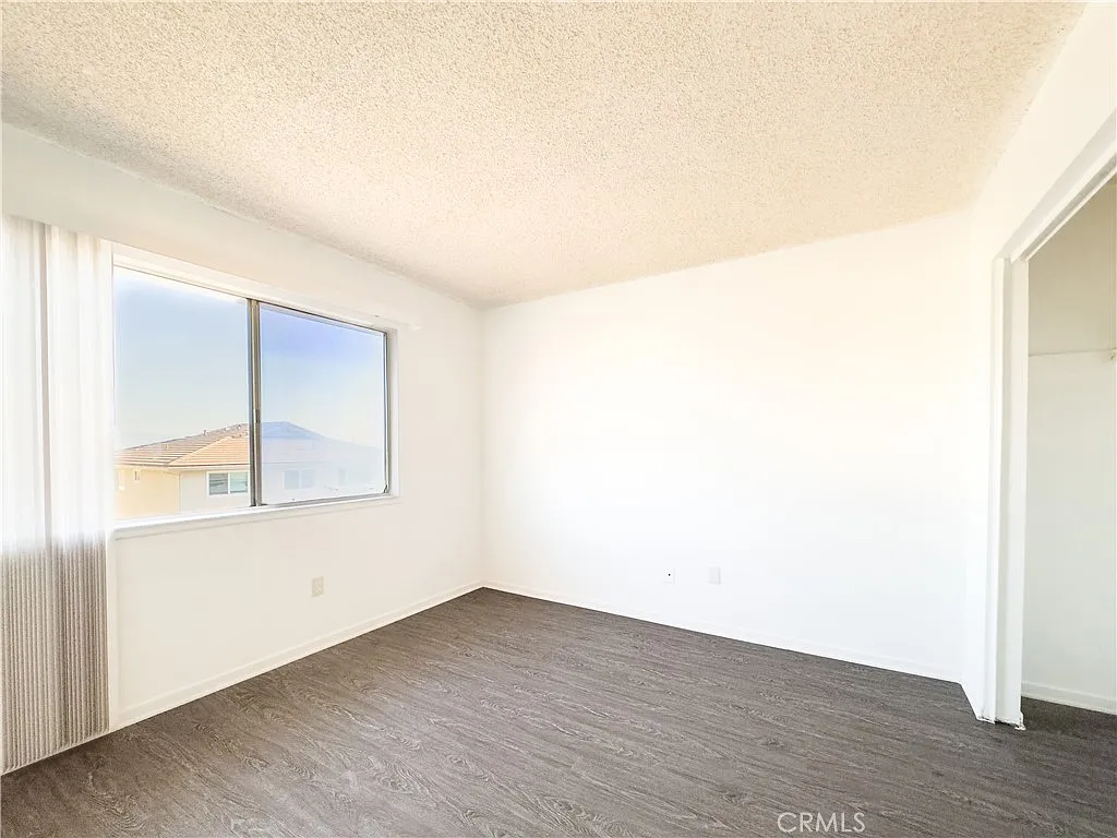 Empty room with light walls, large window, and dark wood floor.