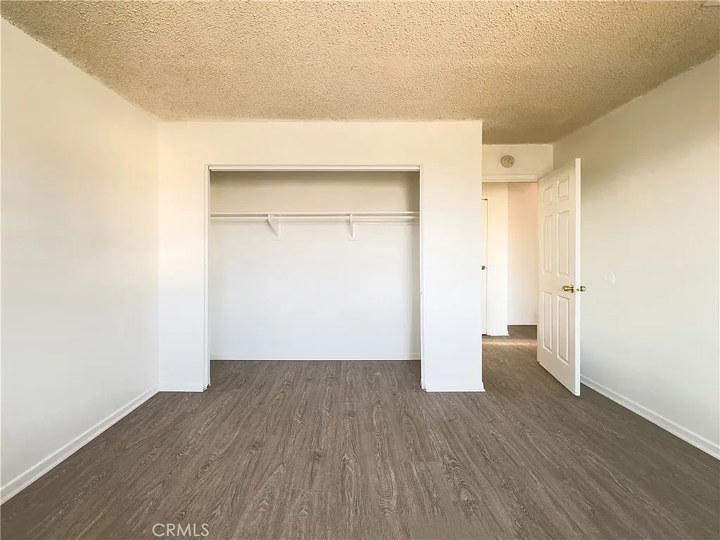 Empty room with light walls, open closet, door to another area, and wood floor.