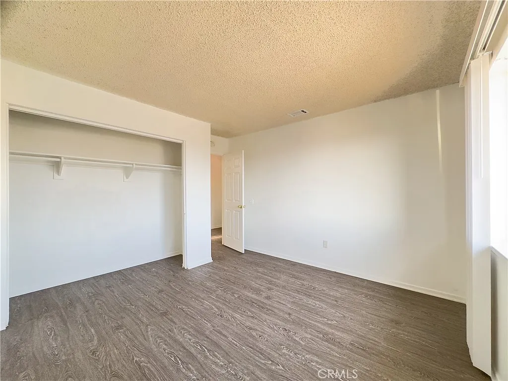 Vacant room with light walls, closet, door to another area, and wooden floor.