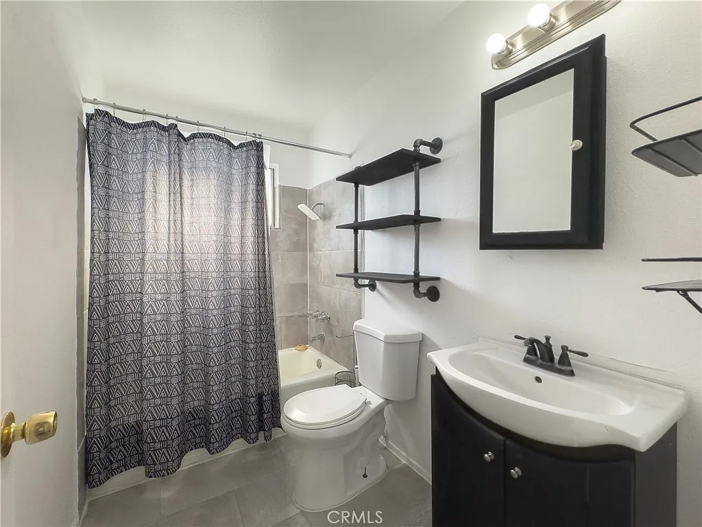 Modern bathroom with shower curtain, white toilet, black shelves, dark sink cabinet, and window light.