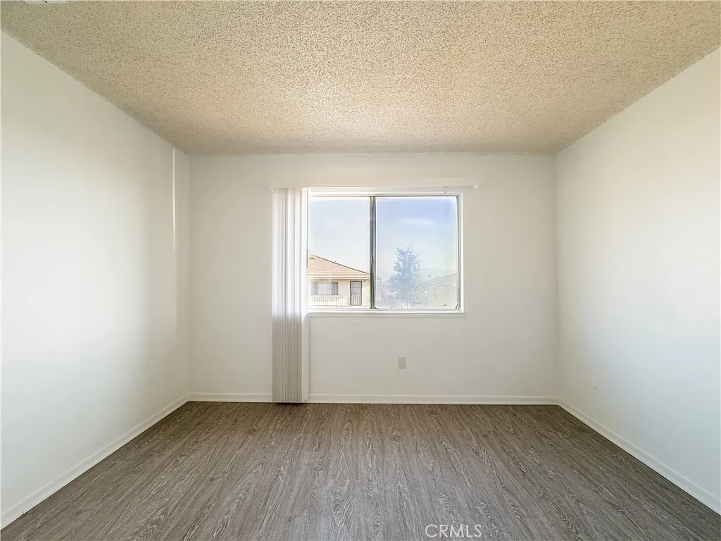 Vacant room with light walls, window, natural light, and wood-like flooring.