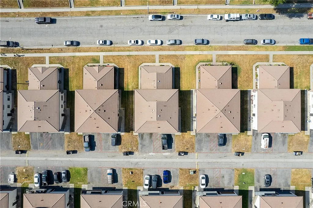 Aerial view of houses with brown roofs in rows, with parked cars on street and driveways.