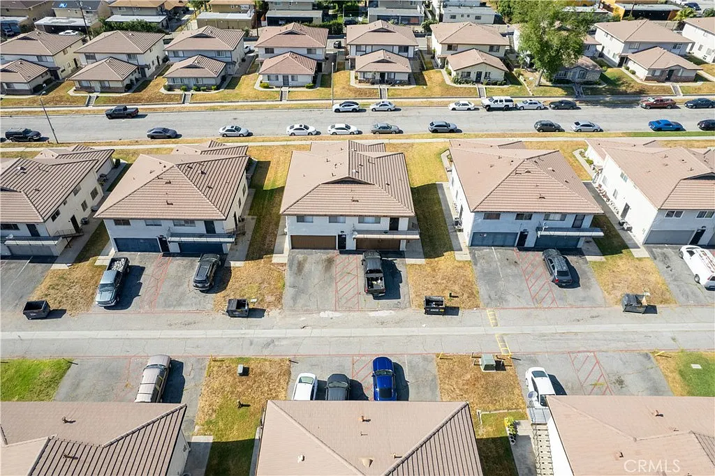 Aerial view of neighborhood with brown roof houses, parked cars, streets, and grassy areas.