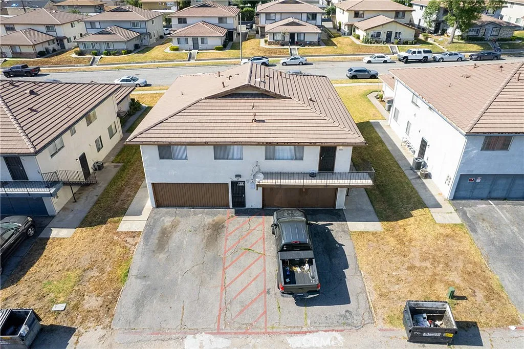 Aerial view of two-story residential building with brown roof, parking spaces, and nearby houses.