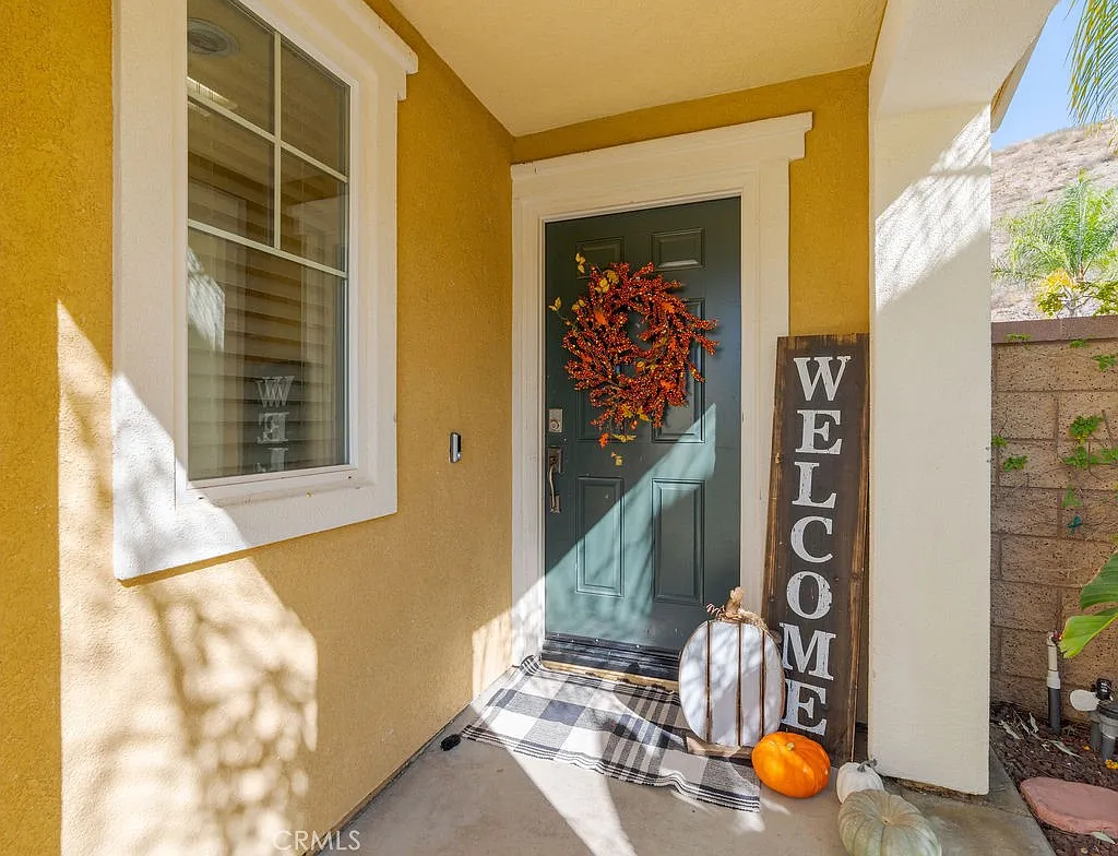 A front porch with green door, wreath, welcome sign, and autumn decorations with pumpkins.