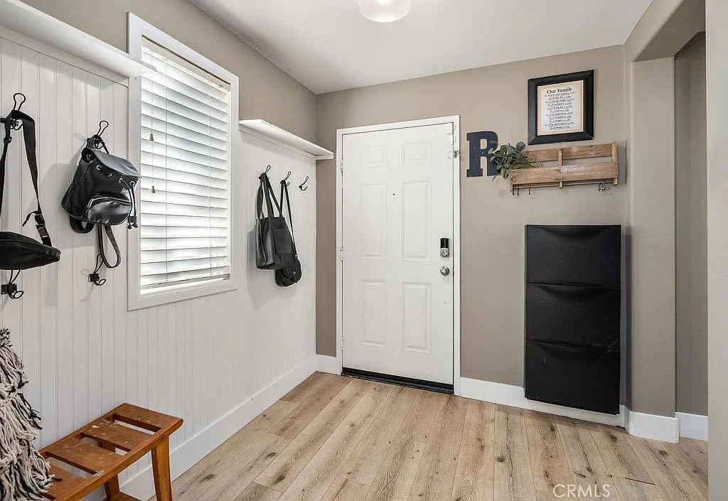 Entryway with front door, wall hooks, small bench, black storage unit, and wood-like floors with neutral walls.