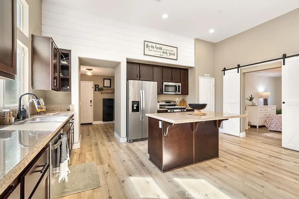 Kitchen with dark cabinets, stainless steel appliances, large island with seating, and light wood floors.