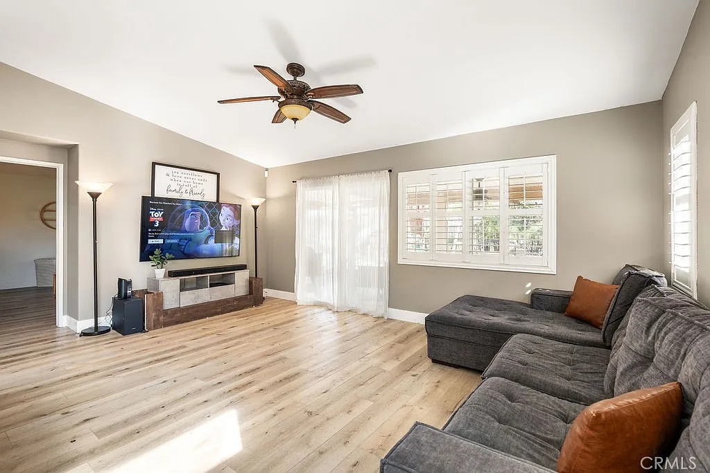Living room with wooden floors, large sofa, wall-mounted tv, and natural light from windows.