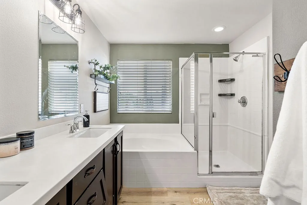 Bathroom with dual sink vanity, dark cabinets, mirror, tub, glass shower, and window.
