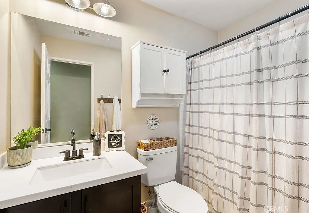 Bathroom with white vanity, sink, mirror, shower curtain, shelf, and plants.