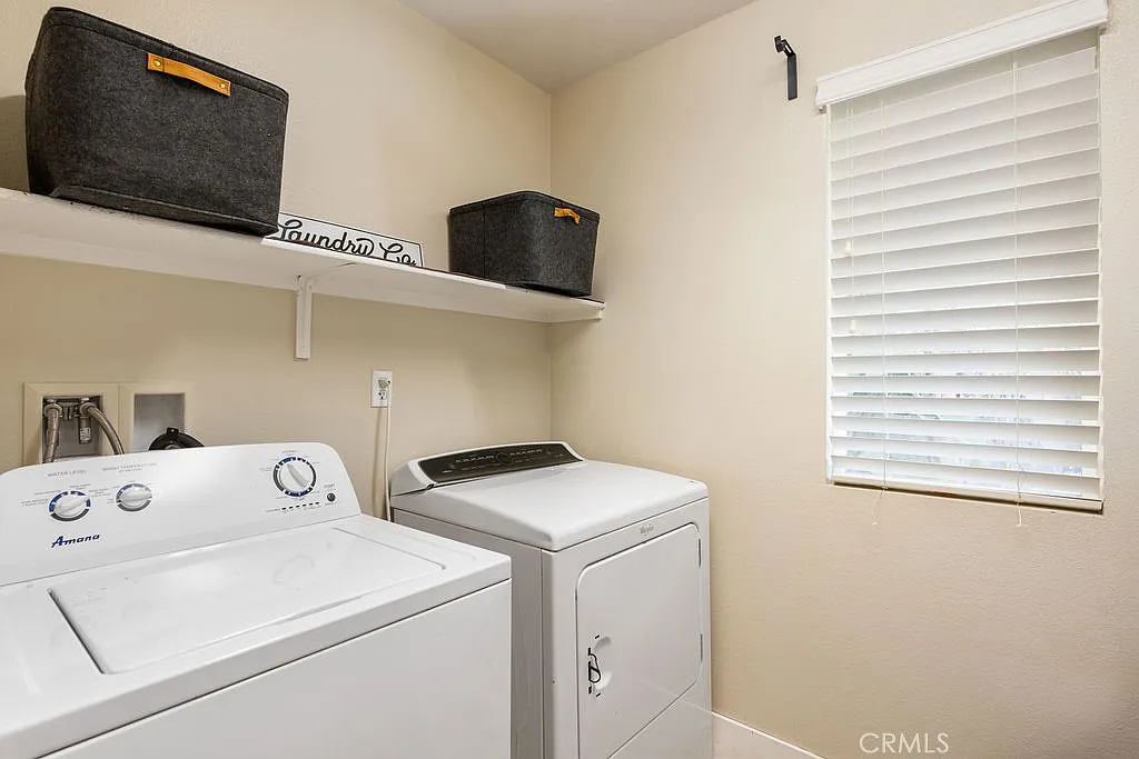 Laundry room with washer, dryer, shelves with baskets, and window blinds.
